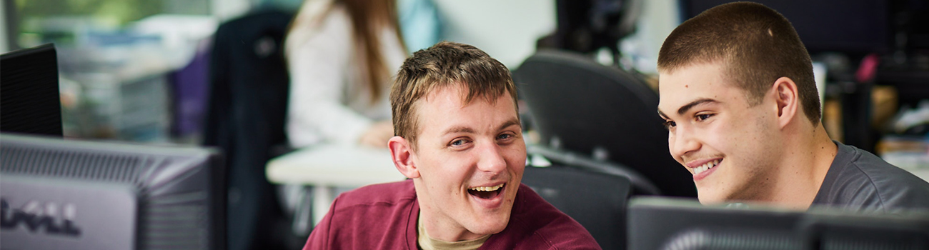 The photo is of two male adults, a participant at Avenue and a support worker, looking at a computer screen smiling