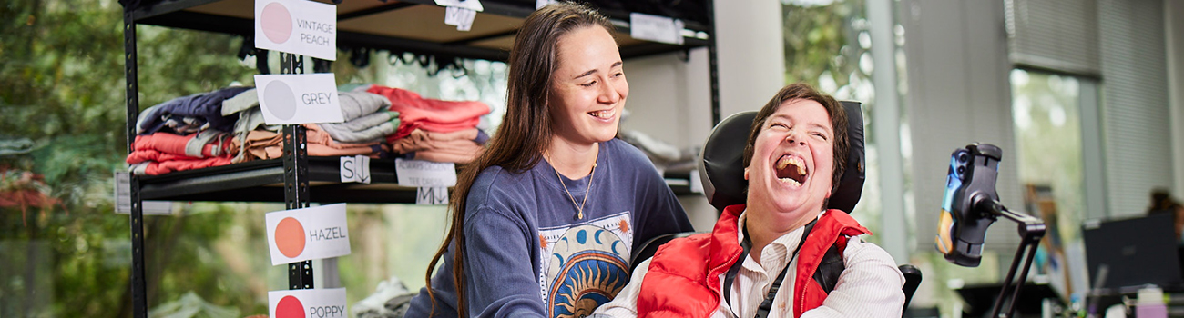 Avenue participant laughing next to her support worker in the Order Fulfilment team