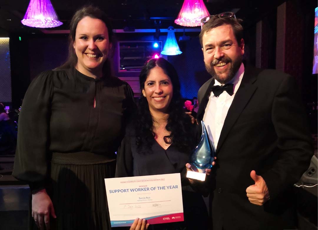 Sonia stands in the middle next to Laura and Adrian, as she holds her award for support worker of the year