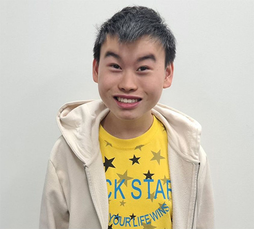 Timothy is smiling at the camera, wearing a yellow t-shirt and cream cardigan.