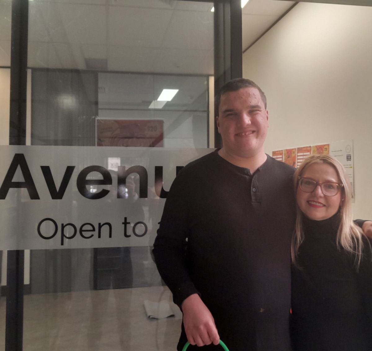 Robert and his mum Julie standing in front of the Avenue sign smiling at camera